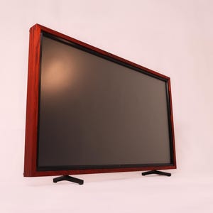 May include: A large, rectangular television with a dark screen and a reddish-brown wooden frame. The TV is supported by two black, angled feet. The screen is dark, and the frame has a visible wood grain.