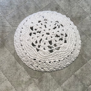 May include: White crocheted doily with a circular design. The doily is made with a delicate, lacy pattern.