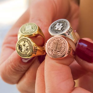 May include: Four gold, silver, and rose gold class rings with the year 2025 engraved on them. The rings feature different university logos and names.