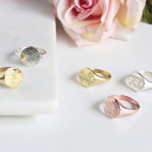 May include: Four signet rings with different initials engraved on the top. The rings are in silver, gold, and rose gold.