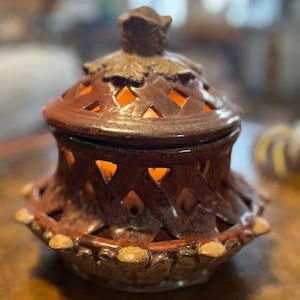 May include: A red clay ceramic candle holder with a lattice design and a lid. The lid has a decorative leaf design.
