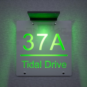 Puede incluir: Letrero de dirección iluminado con el número "37A" y "Tidal Drive" en verde. Montado en una pared gris texturizada, incluye un panel solar. Los números y el texto brillan con una luz verde vibrante.