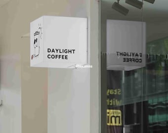 May include: A white sign with black text that reads "Daylight Coffee" and a cartoon illustration of a coffee cup. The sign is mounted on a white wall.