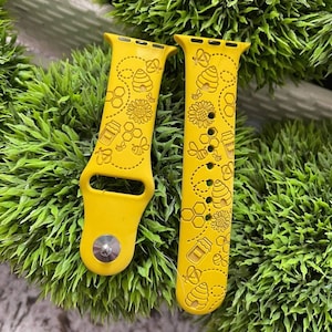 May include: A pair of yellow silicone watch bands with a bee and honeycomb design. The bands are designed for Apple Watch.