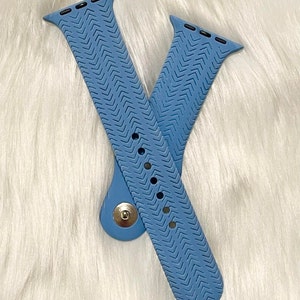 May include: Two light blue watch bands with a chevron pattern. The bands are made of a flexible material and have multiple holes for adjustment. A silver clasp secures the bands together. The bands are designed for a smartwatch.