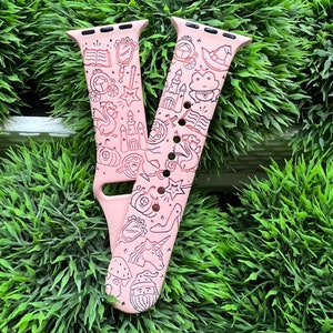 May include: A pink silicone Apple Watch band with a black and white print of fairytale-themed illustrations, including a castle, a crown, a unicorn, a frog, a pumpkin, a star, a wand, and a book.