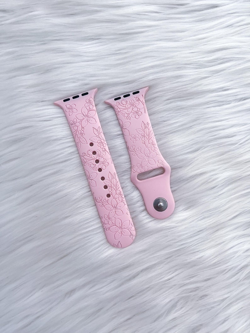 May include: A pair of pink silicone watch bands with a floral design. The bands are designed for Apple Watches.