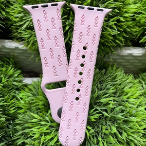 May include: Pink Apple Watch band with a repeating pattern of small pine trees. The band is made of silicone and has a smooth finish.