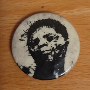 Peut inclure: Un bouton noir et blanc représentant un portrait rapproché d'une personne avec une coiffure hérissée.