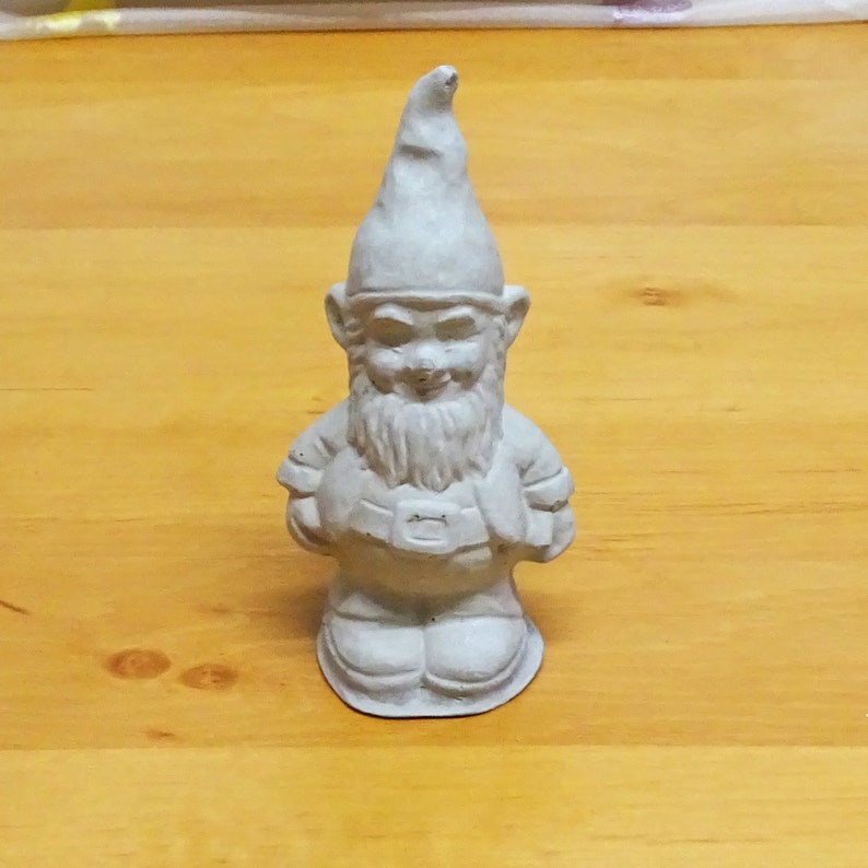 May include: A white ceramic garden gnome figurine with a pointed hat, a beard, and a belt. The gnome is smiling and has a friendly expression.