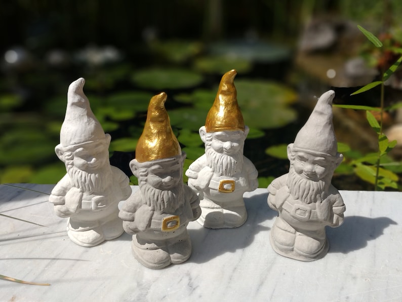 May include: Four white garden gnomes with gold accents. The gnomes are standing on a white surface.