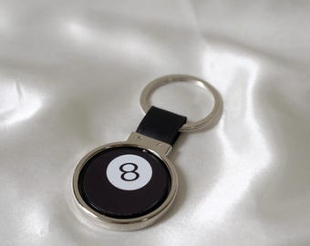May include: A silver keyring with a black leather strap and a round black and white 8-ball design.