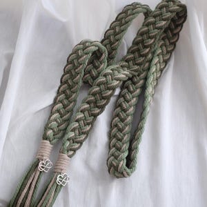 Op de afbeelding: Twee gevlochten koorden in groen en beige met zilveren hartvormige bedels aan de uiteinden.