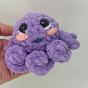 May include: A purple crocheted octopus with black eyes and pink cheeks. The octopus has eight tentacles.