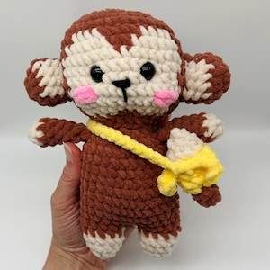 May include: A handmade crochet monkey doll in brown, cream, and yellow. The monkey has black eyes, pink cheeks, and a yellow banana bag. The doll is made of soft yarn and has a cute, friendly expression.