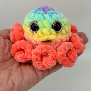 May include: A rainbow crocheted octopus with large black eyes and a pink body. The octopus is made with soft yarn and has a friendly expression.