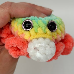 May include: A crocheted rainbow octopus with large black eyes and a clear bubble filled with white beads.