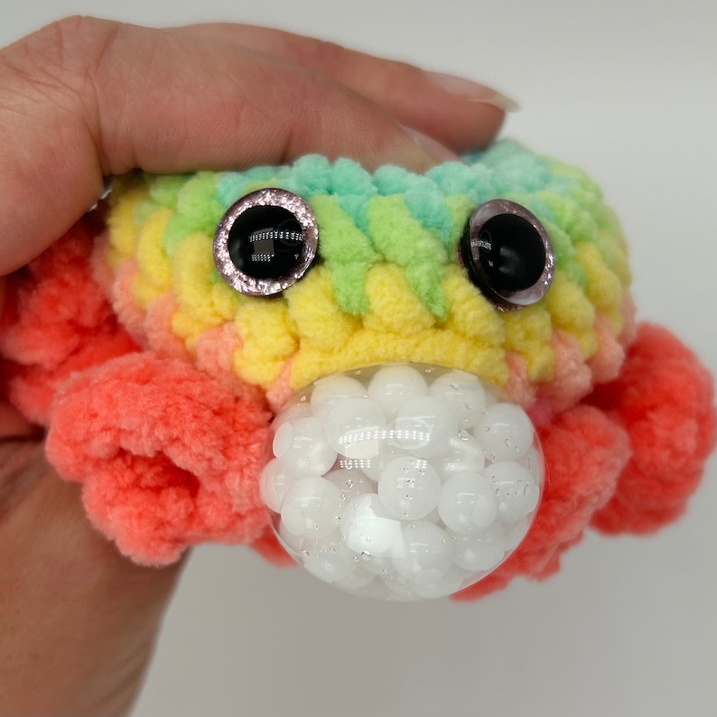 May include: A crocheted rainbow octopus with large black eyes and a clear bubble filled with white beads.