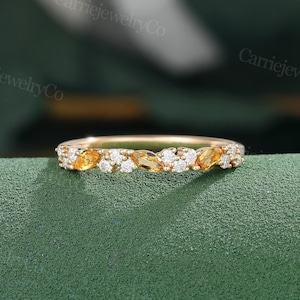 May include: A delicate gold band ring featuring a row of alternating marquise-shaped citrine and round diamonds. The ring is displayed on a green fabric background.