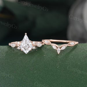 May include: A rose gold engagement ring set featuring a kite-shaped center stone flanked by small marquise and round accent diamonds, paired with a matching curved wedding band adorned with marquise-cut diamonds along the band's top edge.