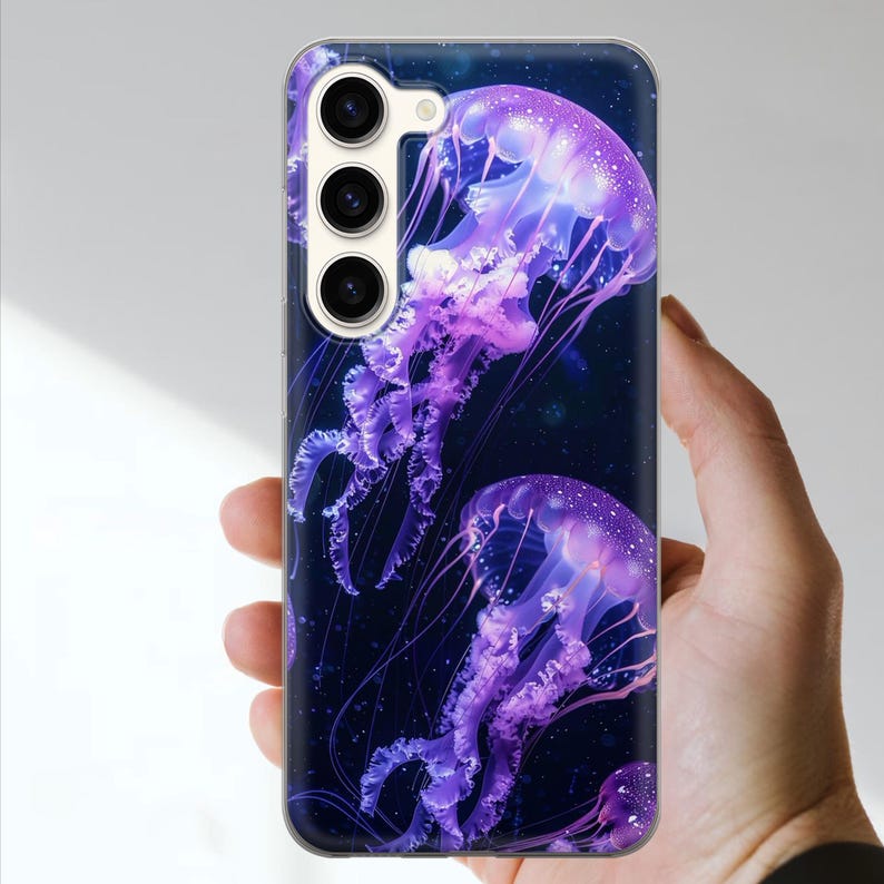 May include: A phone case featuring a vibrant design of purple jellyfish against a dark blue background. The case has a clear border and a camera cutout. The jellyfish have detailed tentacles and a glowing effect.