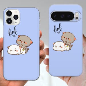 May include: Two light blue phone cases with a cartoon cat design. One case is for an iPhone, the other for a Google Pixel. The design features two cartoon cats, one gray and one white, with the text "bad girl".