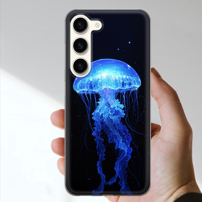 May include: A phone case featuring a vibrant blue jellyfish design against a dark background. The jellyfish has a glowing, ethereal appearance with long, flowing tentacles. The case has a clear border and a camera cutout.