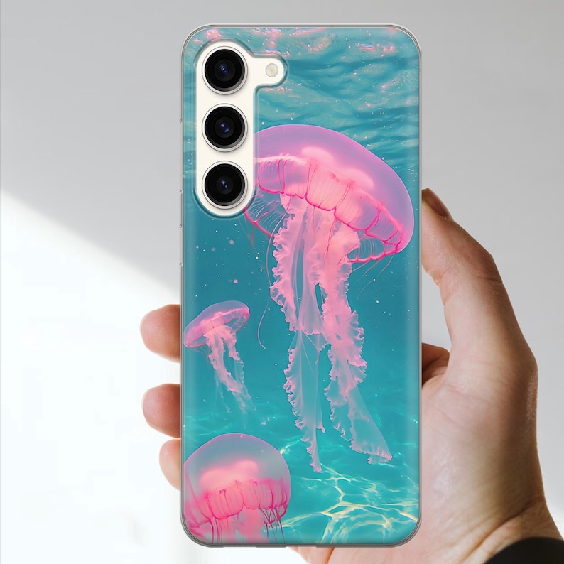 May include: A phone case featuring a vibrant underwater scene with pink jellyfish floating in turquoise water. The case has a clear, glossy finish and a camera cutout.