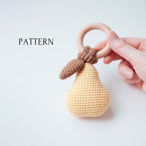 以下が含まれることがあります： 木製の歯固めリングに茶色の葉がついた、かぎ針編みで作った洋梨の形をしたおもちゃ。おもちゃは黄色と茶色です。