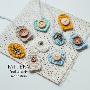 May include: A collection of crocheted heart and oval shapes with various buttons and embellishments. The crocheted pieces are displayed on a fabric with a brown and white polka dot pattern. The text "PATTERN *not a ready made item" is visible at the bottom of the image.