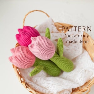 Op de afbeelding: Een gehaakt boeket van drie roze tulpen met groene stelen en bladeren. De tulpen bevinden zich in een rieten mand die is bekleed met witte kant. De tekst "PATTERN * not a ready made item" is zichtbaar in de afbeelding.