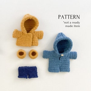 May include: Two crocheted hooded jackets, one yellow and one blue, with matching crocheted booties and shorts. The jackets have a button closure and the shorts have a ruffled hem. The text "PATTERN *not a ready made item*" is displayed above the jackets.