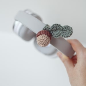 May include: A crocheted acorn charm with a green leaf attached to a pair of gray headphones.