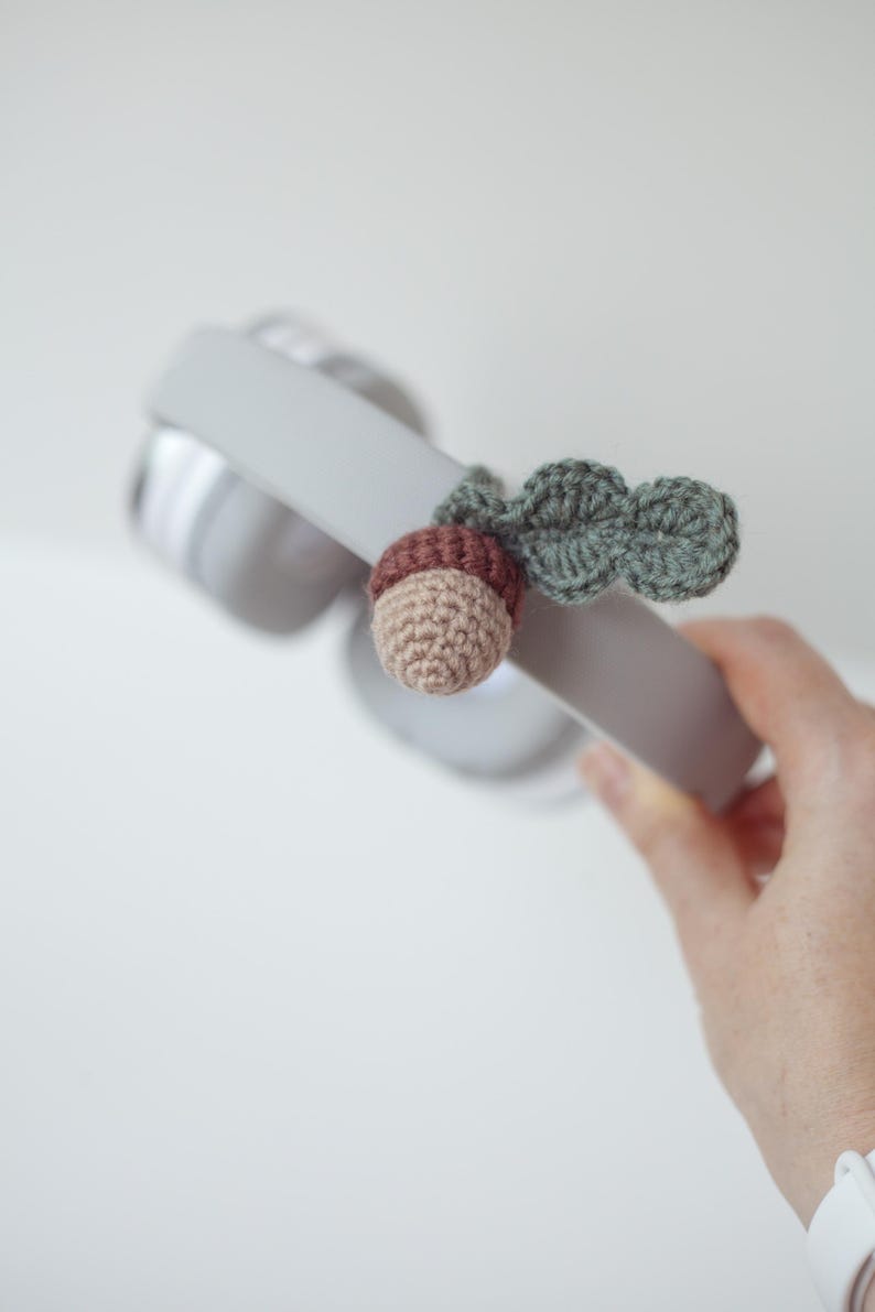 May include: A crocheted acorn charm with a green leaf attached to a pair of gray headphones.