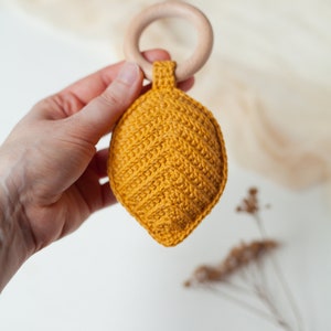 May include: A yellow crocheted leaf-shaped baby rattle attached to a wooden ring.