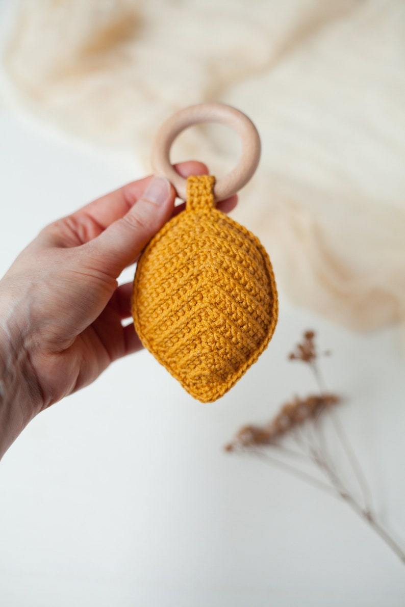May include: A yellow crocheted leaf-shaped baby rattle attached to a wooden ring.