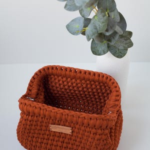 May include: A rust-colored crocheted storage basket with a leather label that says "Handmade with Love".