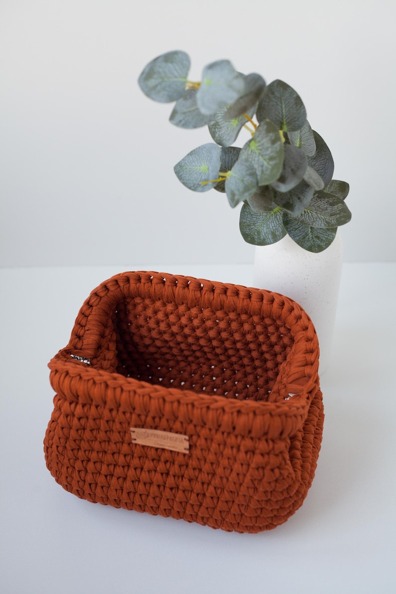 May include: A rust-colored crocheted storage basket with a leather label that says "Handmade with Love".