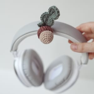 May include: White headphones with a crocheted acorn charm attached to the headband. The acorn is brown and green.