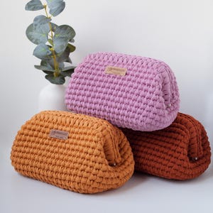 May include: Three crocheted pouches in different colors: pink, orange, and brown. Each pouch has a small leather tag with the word "remarkable" on it.