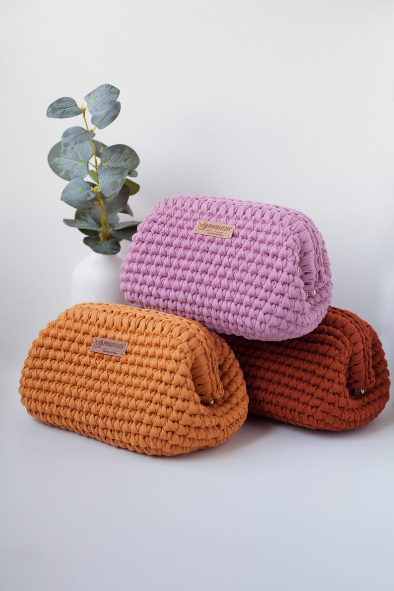 May include: Three crocheted pouches in different colors: pink, orange, and brown. Each pouch has a small leather tag with the word "remarkable" on it.