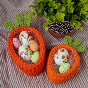 May include: Two orange crocheted carrot-shaped baskets filled with colorful Easter eggs. The baskets are on a brown and white checkered tablecloth.