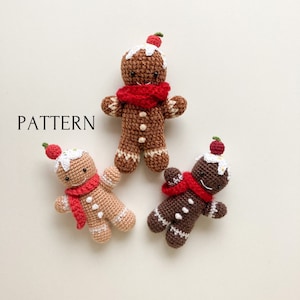 May include: Three crocheted gingerbread people with red scarves and white icing. The gingerbread people are brown, tan, and dark brown.