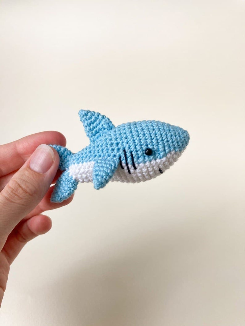 May include: A small crocheted blue shark toy with white accents and black eyes.
