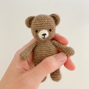May include: A small brown crocheted teddy bear with black eyes and a white nose.
