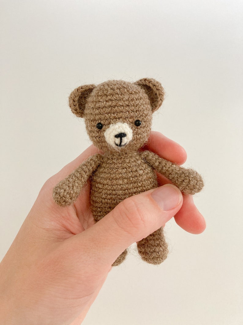 May include: A small brown crocheted teddy bear with black eyes and a white nose.