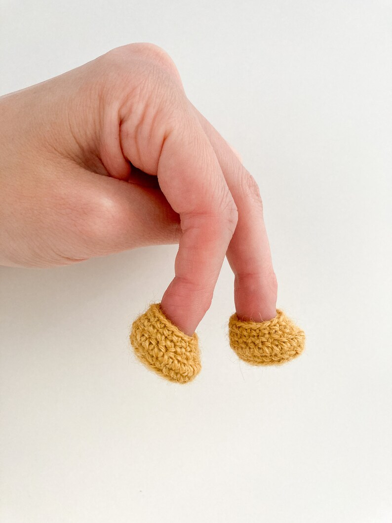 May include: Two crocheted fingertip covers in a mustard yellow color. The covers are worn on two fingers of a hand.