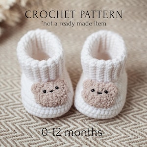 May include: White crocheted baby booties with a brown bear face on the front. The booties are for ages 0-12 months. The text "CROCHET PATTERN * not a ready made item" is above the booties.