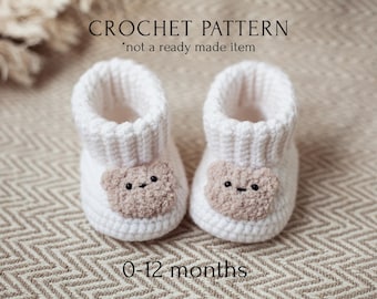 May include: White crocheted baby booties with a brown bear face on the front. The booties are for ages 0-12 months. The text "CROCHET PATTERN * not a ready made item" is above the booties.