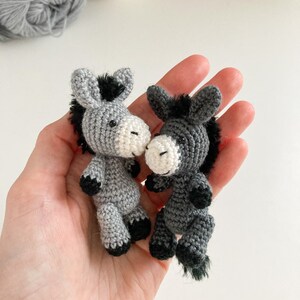 May include: Two gray crocheted donkey figurines with black manes and tails. The donkeys are facing each other and have white faces.